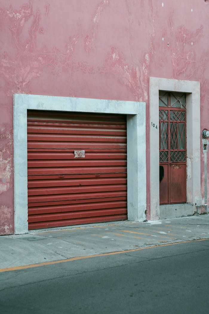 Close-up of a faded red garage and door on a pink wall in Aguascalientes, Mexico, showcasing urban decay.